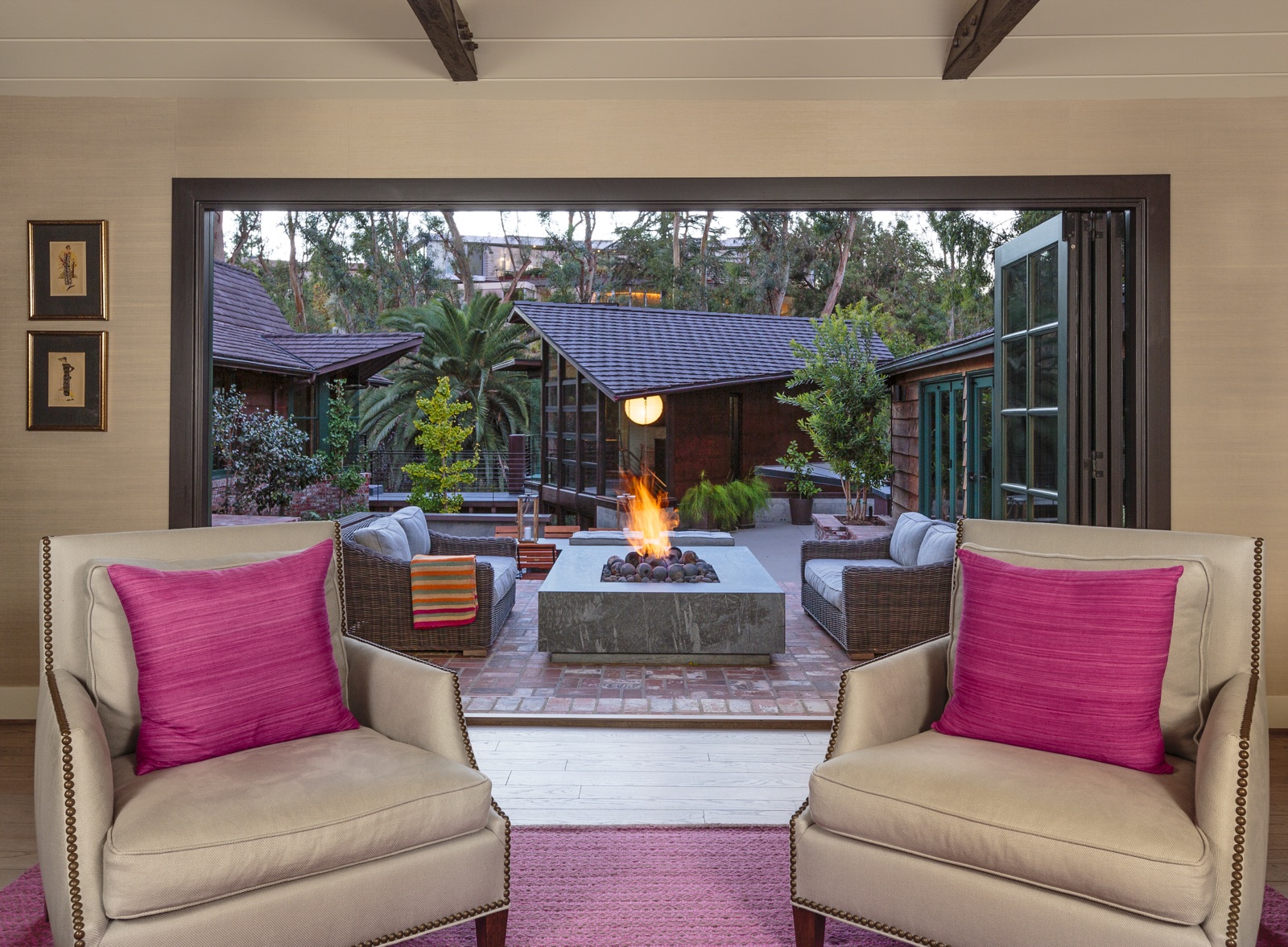 Indoor-outdoor living: full-height bi-fold doors opening to a brick-paved fire pit terrace and guest cottage. Luxury custom residence built by ESRL Development.