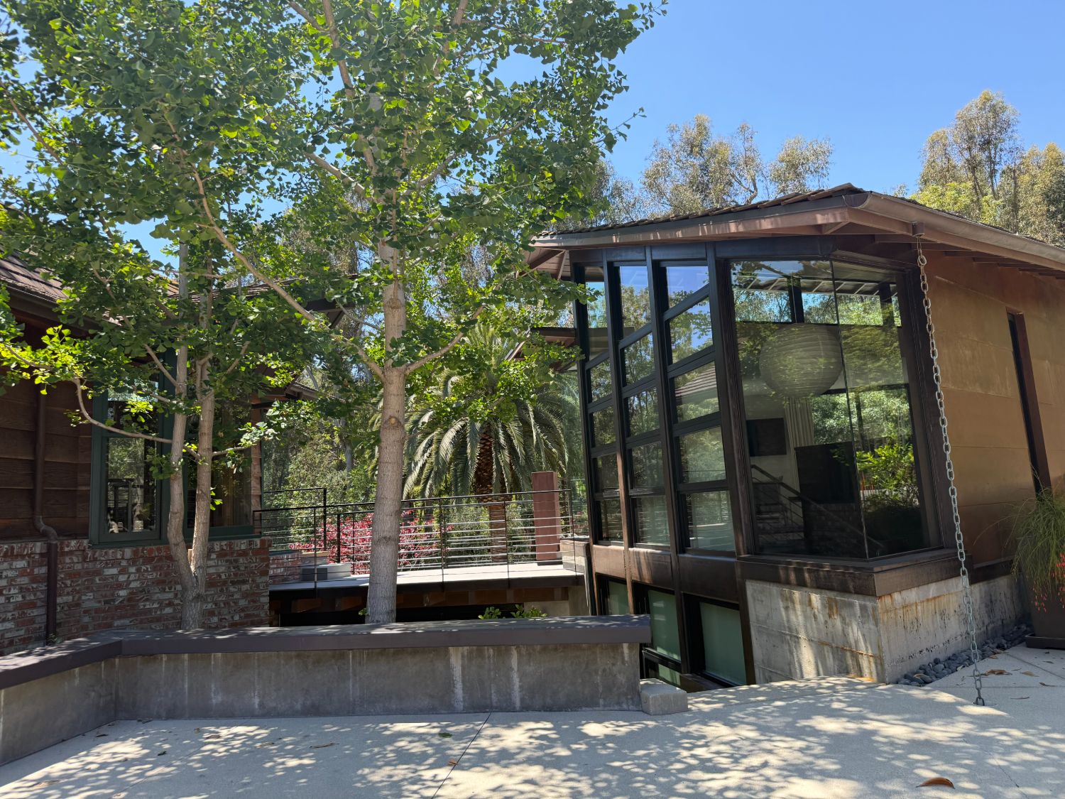 Brentwood custom residence by ESRL Development, exterior view of the glass-and-steel pavilion with hand-built window frames, cedar-sided wing, brick base, mature gingko and palm trees.