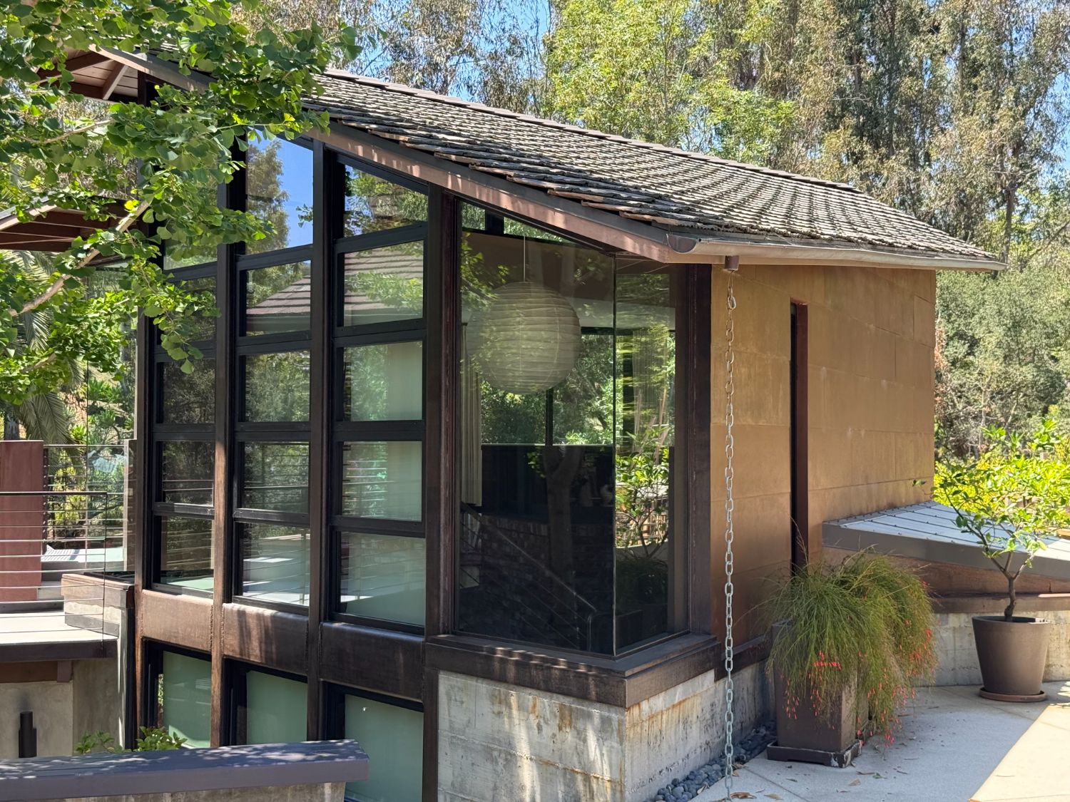Corner view of the glass-and-steel pavilion with Japanese kusari-doi rain chain and slate-tile roof. Brentwood, ESRL Development.