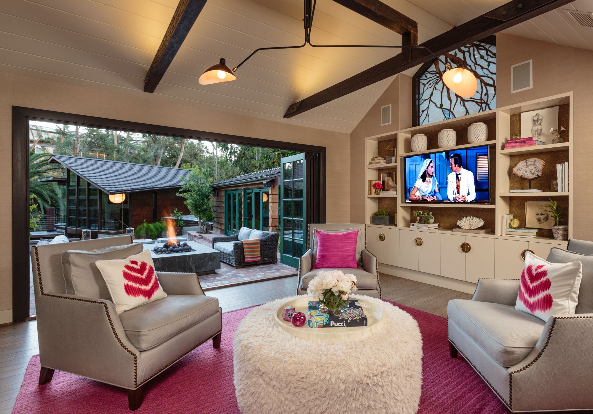 Brentwood interior, vaulted shiplap ceiling, dark exposed beams, sputnik chandelier, looking out through open bi-fold doors to the courtyard and glass-and-steel pavilion. ESRL Development.
