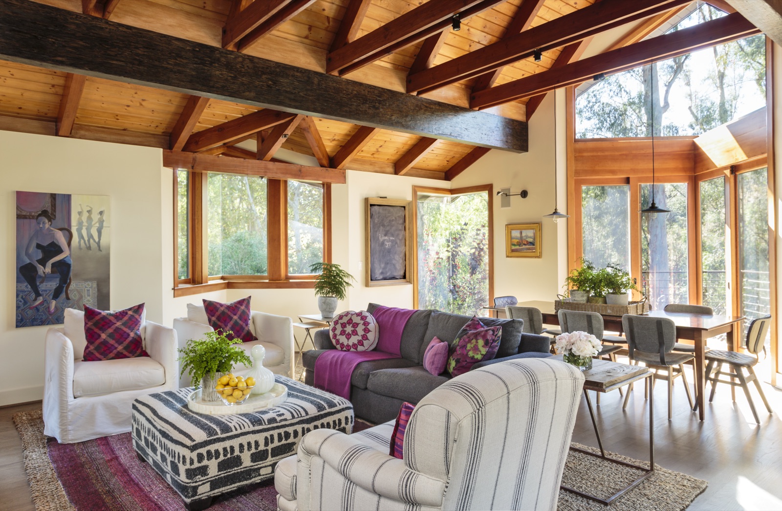 Brentwood Layton Drive great room, exposed rough-sawn timber trusses, full wall of glass to the canyon, plum and ivory upholstery, dining beyond. Custom luxury residence by ESRL Development.