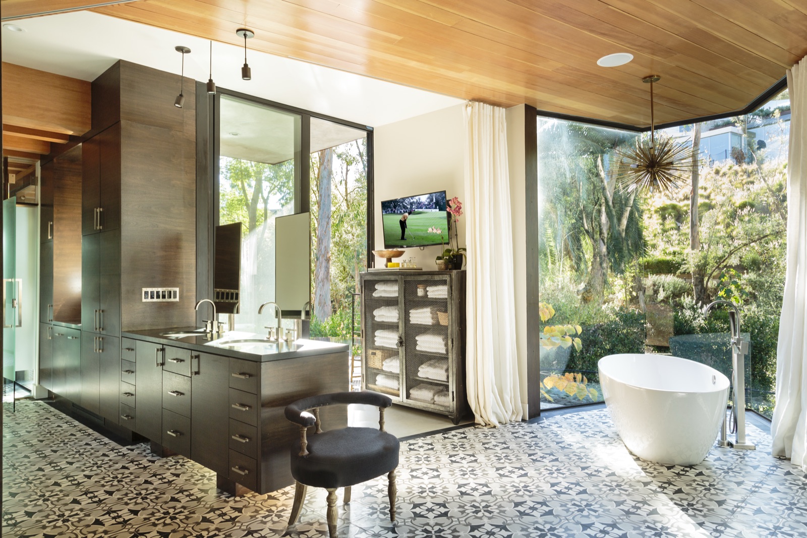 Master bathroom in the Brentwood Layton Drive residence, patterned cement-tile floor, freestanding sculptural soaking tub, full-height glass to a private walled garden, dark-stained double vanity and cedar ceiling. ESRL Development.