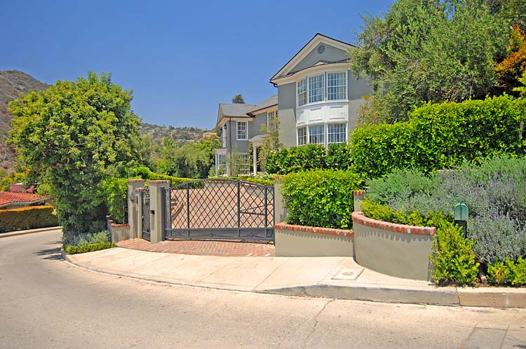 Custom wrought-iron entry gate, scalloped stucco garden wall with brick capping, hand-laid brick driveway. Hollywood Hills.
