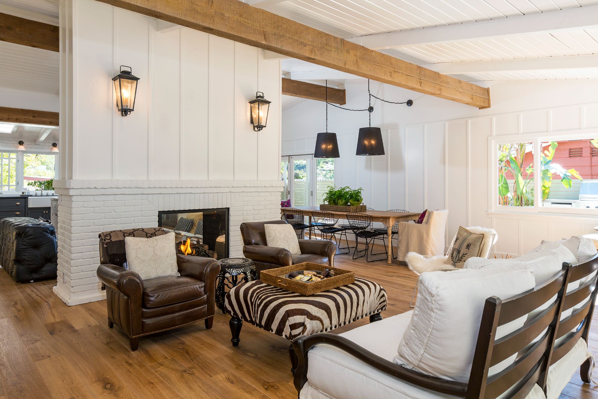 Great room with double-sided painted-brick fireplace, vintage lantern sconces, leather club chairs, zebra ottoman, vaulted shiplap ceiling. Pacific Palisades beach house remodel.