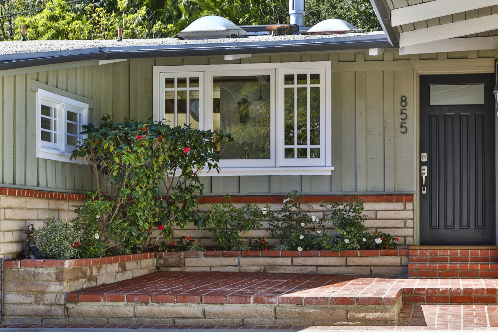 855 Jacon Way Pacific Palisades entry detail, restored board-and-batten siding in soft sage, painted-brick stoop, custom white casement window with divided lites, glass-paneled dark-bronze front door. ESRL Development.