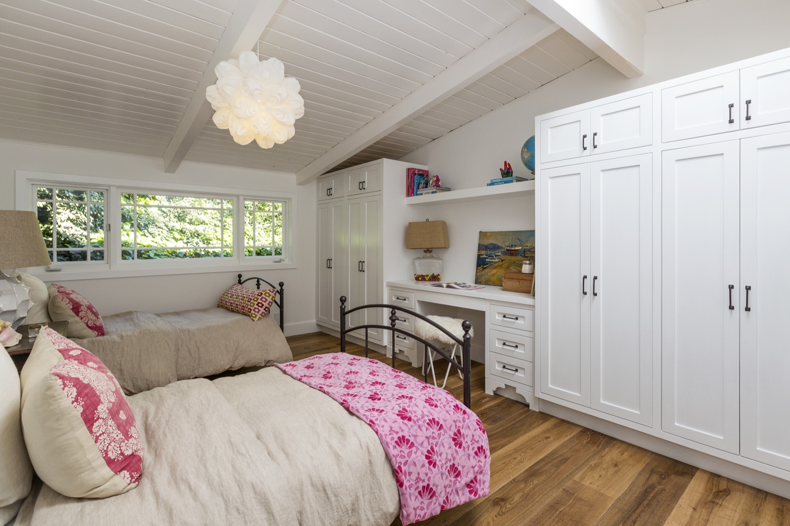 Guest bedroom at 855 Jacon Way Pacific Palisades, vaulted plank ceiling, twin metal beds, custom wall-to-wall white wardrobes with shaker-doors flanking a built-in study desk under casement windows. ESRL Development built-ins.
