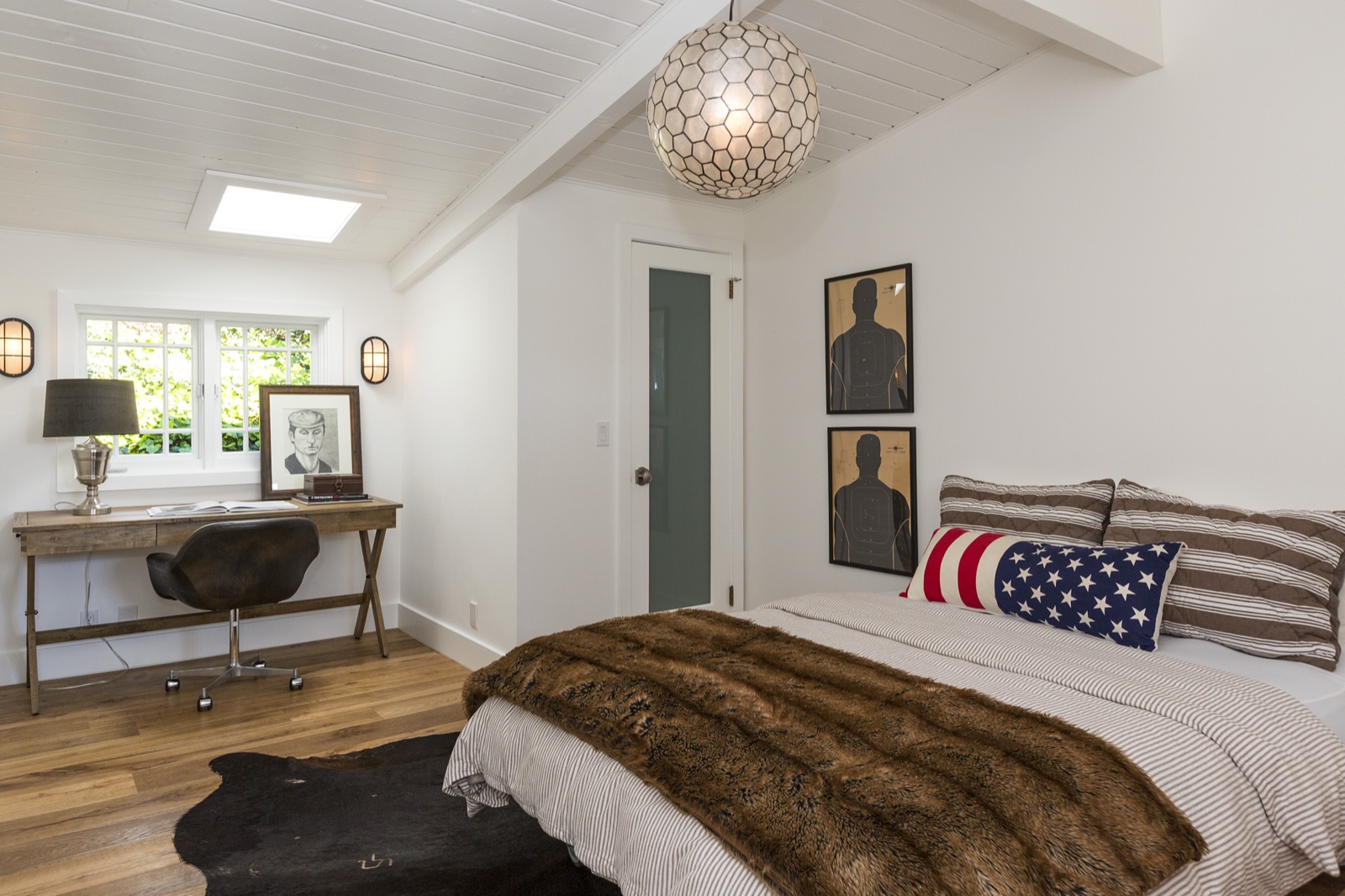Guest bedroom and reading nook at 855 Jacon Way Pacific Palisades, twin skylights overhead, blue-and-white slipper chairs, walnut writing desk on a yellow-patterned rug. Coastal beach-cottage remodel by ESRL Development.