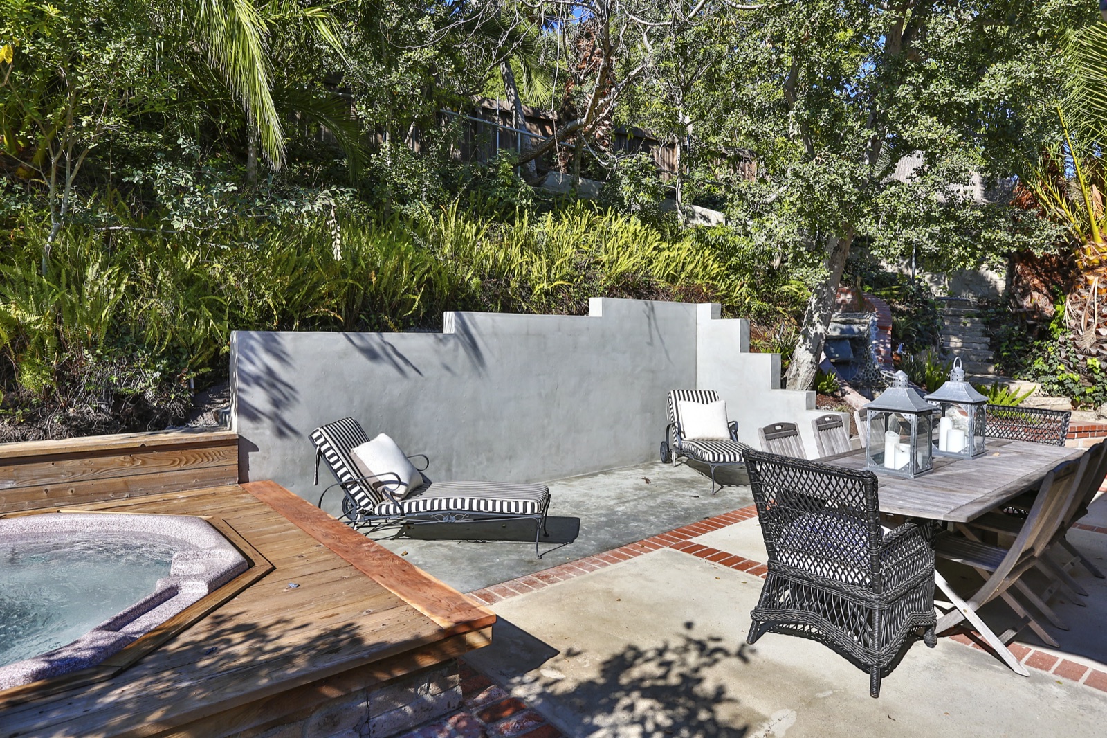 Backyard at 855 Jacon Way Pacific Palisades, sunken hot-tub spa set into a wood deck, black-and-white striped chaise lounges, a hand-laid brick patio with banded inlay, a stepped stucco retaining wall against the Palisades canyon hillside. ESRL Development.